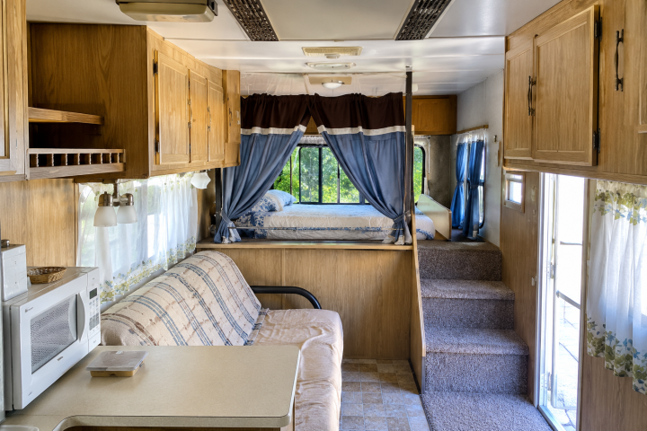 Interior of an RV with couch, microwave, cabinets, and bed in the rear.