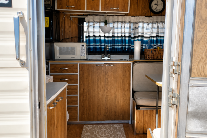 Interior of a small wooden RV kitchen with microwave and seating area.