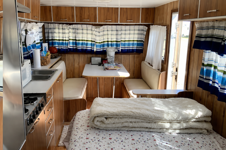 Interior of a cozy camper with kitchen, table, benches, and bed.