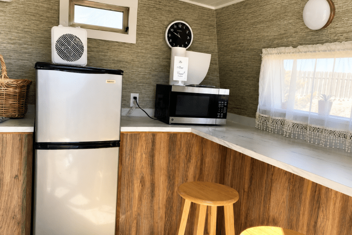 Small kitchen area with fridge, microwave, and two wooden stools.