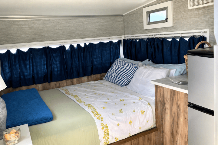 Cozy RV interior with a bed, blue curtains, and a small kitchenette.