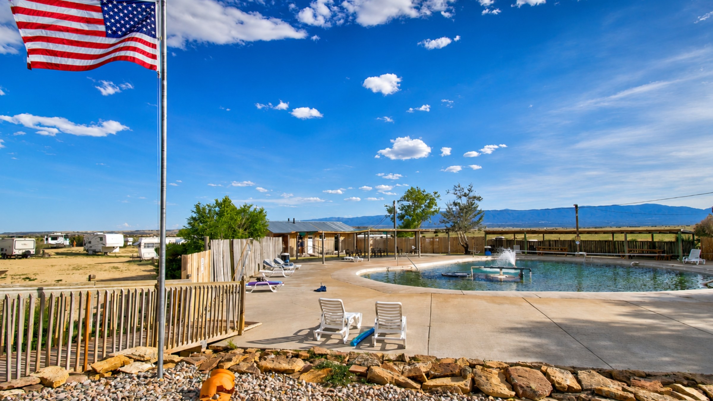 Pool area with American flag, lounge chairs, and cloudy sky.