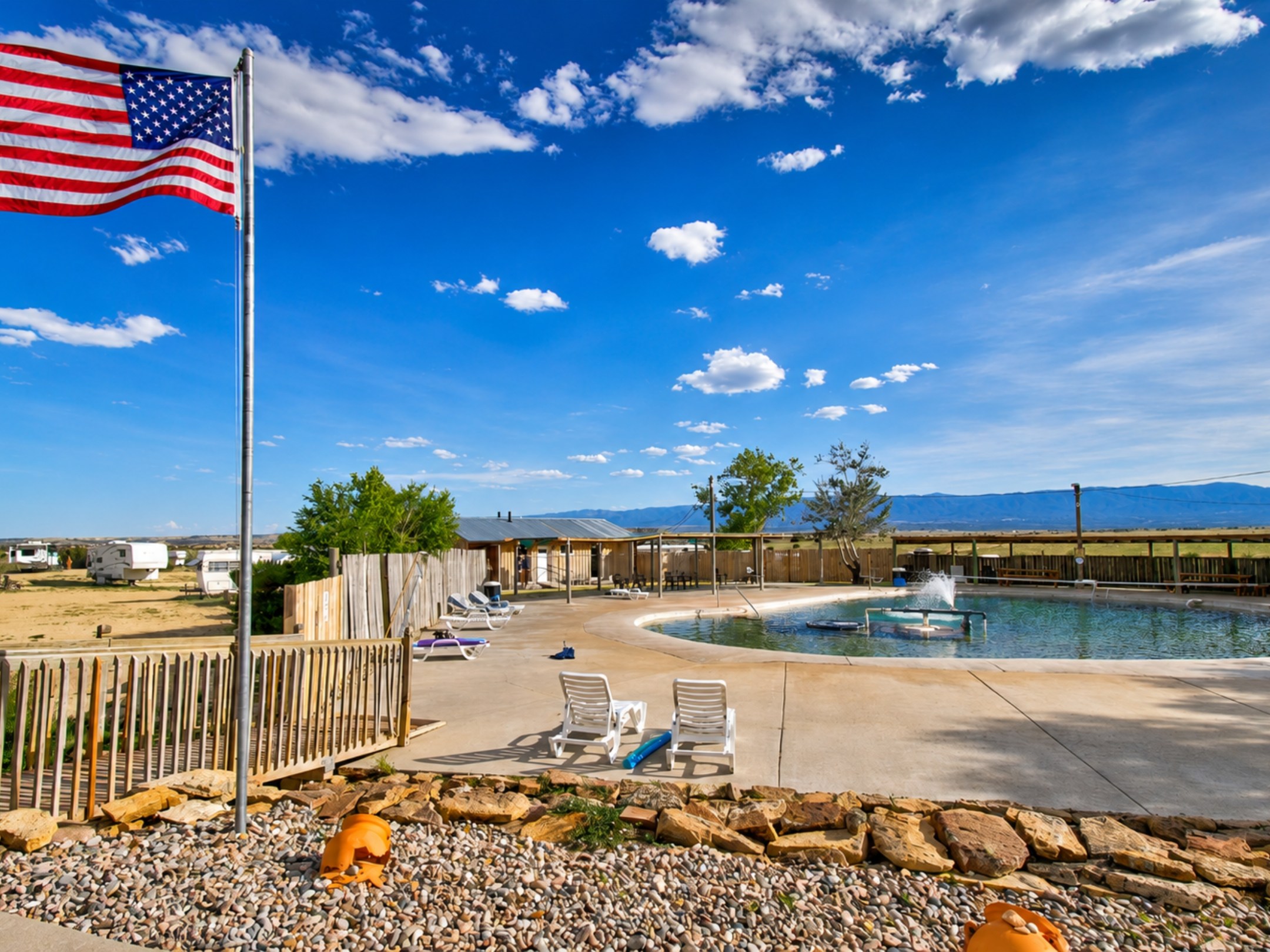 Pool area with American flag, lounge chairs, and cloudy sky.