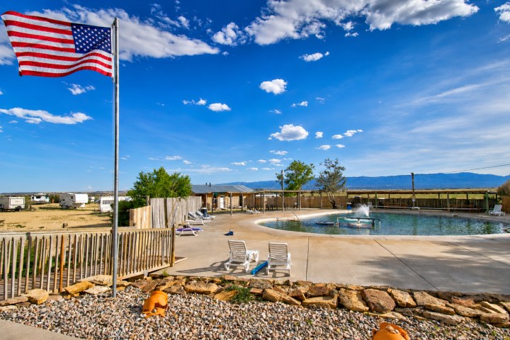 Pool area with American flag, lounge chairs, and cloudy sky.