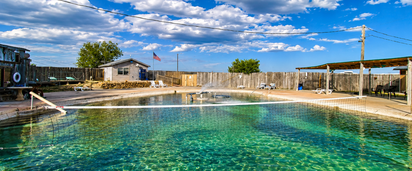 Outdoor swimming pool with a net, surrounded by fence, clear sky with clouds.